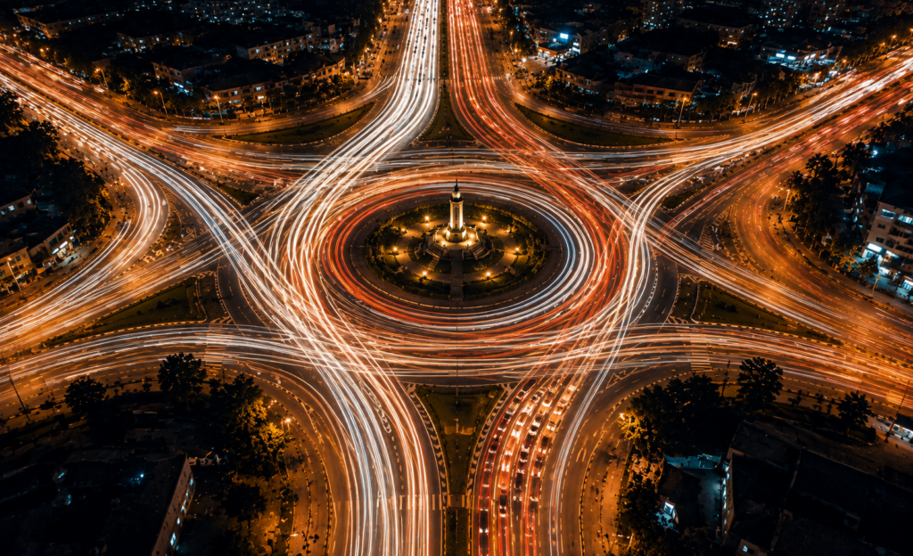 Long-exposure aerial view of a busy roundabout with continuous traffic circling a brightly lit center, symbolizing the continuous customer lifecycle from prospect to expansion.